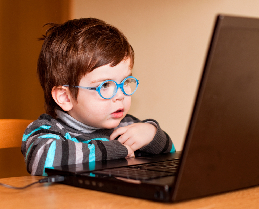 Young boy with blue glasses reading at a computer