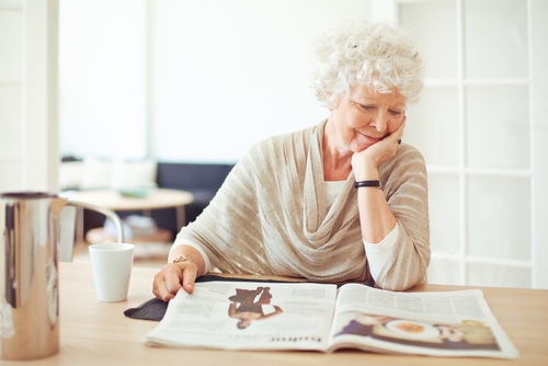 Older woman reading newspaper at table 