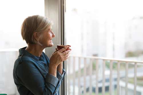 Smiling older woman holding coffee cup while looking out window